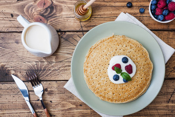 Plate of delicious thin pancakes with berries on wooden table Copy space