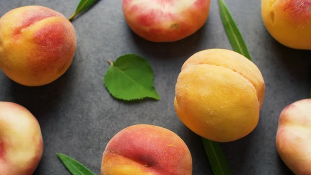Nice yummy fresh peaches with green tree leaves on dark texture surface. Top view. Summer fruits. 4k.