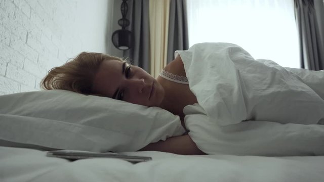 Sleepy woman turns alarm off while awakening in the morning.