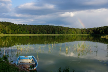 nordic summer lake in soft evening mood with rainbow and boat