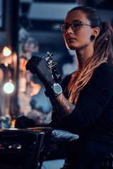 Young attractive tattoo artist in black gloves is tuning her tattoo machine before tattoo session.