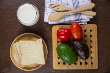 Top view sliced bread toped with condensed milk on wooden plate and fresh milk, tomato,avocado on breakfast healthy and diet food concept