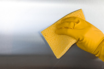 Hand with rubber glove cleaning metal kitchen surface.