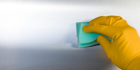 Hand with rubber glove cleaning metal kitchen surface.