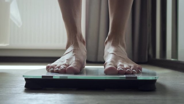 Unrecognizable woman stands on floor scale in the bedroom.