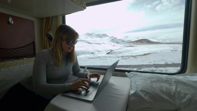 CLOSE UP: Female traveler writing her travel blog while travelling by train across the snow covered landscape of Himalaya. Busy woman answering work emails during her train journey across Tibet.