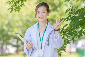 手で「3」のポーズをする白衣の女性
