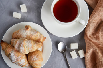 cup of tea, croissants, sugar cubes on a gray background, view from above