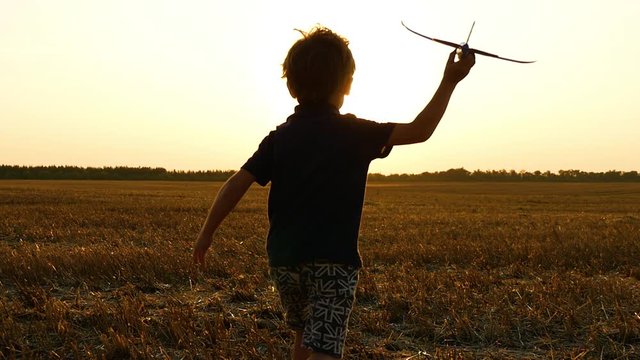 The boy runs through the wheat field after the harvest. The child holds a toy plane in his hand and imagines flying. Victory, achievement of goals and motivation.