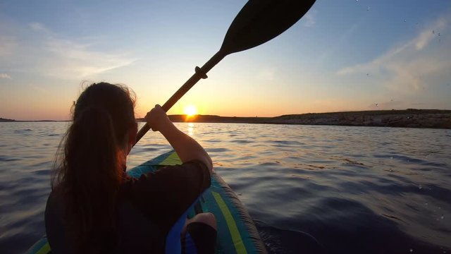 Woman paddling her kayak towards the setting sun