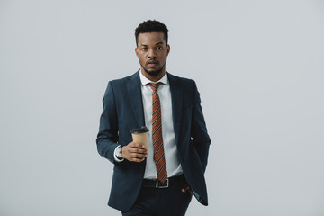 handsome african american businessman holding with hand in pocket and holding paper cup isolated on grey