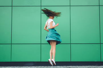 Young women dressed in white topic and turquoise skirt with coral bag jumping near grey street backgraund. Fashion and stylish concept.