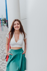Young women dressed in white topic and turquoise skirt with coral bag, on grey street backgraund....