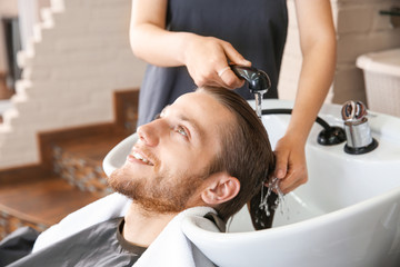 Female hairdresser washing hair of young man in salon