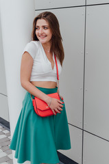 Young women dressed in white topic and turquoise skirt with coral bag, on grey street backgraund....