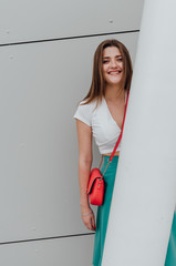 Young women dressed in white topic and turquoise skirt with coral bag, on grey street backgraund. Fashion and stylish concept.