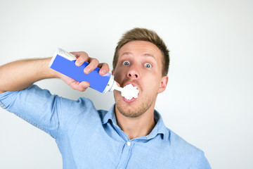 young handsome man sprays whipped cream directly to his mouth looking surprised on isolated white...