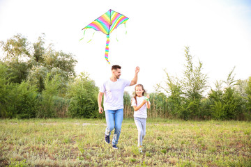 Young man with little daughter flying kite outdoors