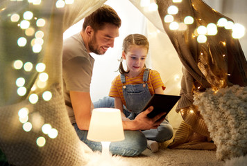 family, hygge and technology concept - happy father and little daughter with tablet pc computer in kids tent at night at home © Syda Productions