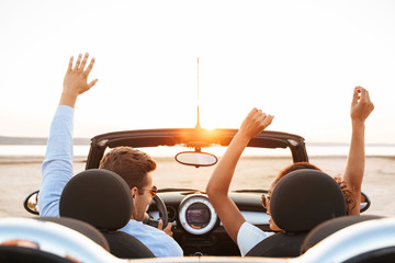 Image from back of beautiful multiethnic couple rejoicing while driving convertible stylish car by...