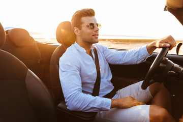 Photo of beautiful caucasian man driving convertible car by seaside at sunrise