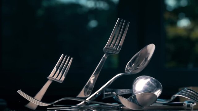 Bunch of spoons, forks and knives fall down on the table, super slow motion shot