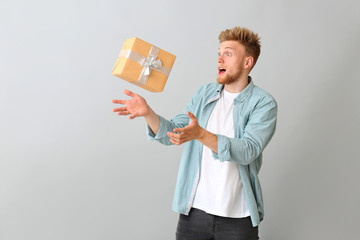 Young man catching gift box on light background