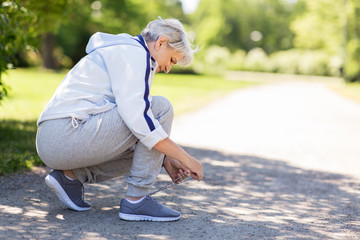 fitness, sport and healthy lifestyle concept - senior woman tying shoe laces at summer park - obrazy, fototapety, plakaty