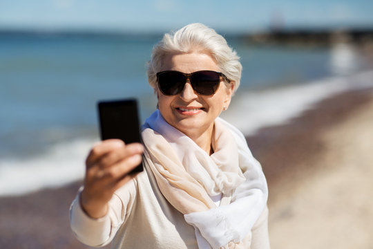 old people and leisure concept - happy smiling senior woman taking selfie by smartphone on beach in estonia