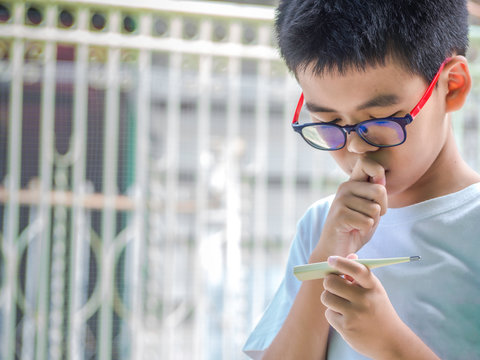 Asia Boy Measuring Temperature Of Himself Ill. Sick Child With High Fever And Holding Thermometer.