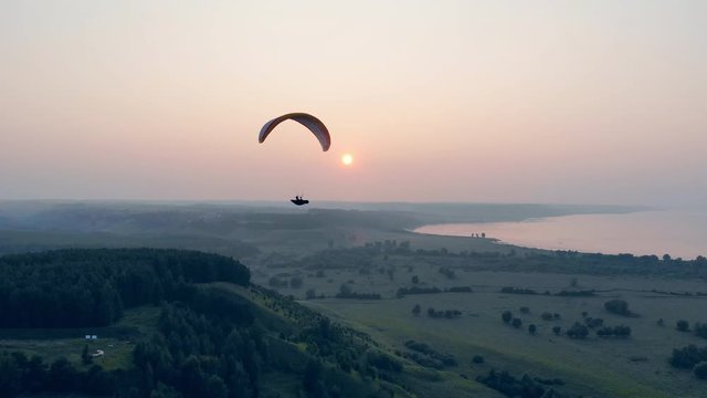 Paraglider in the sky. Airsailing vehicle is drifting above green landscape . Parachute, paragliding comcept.