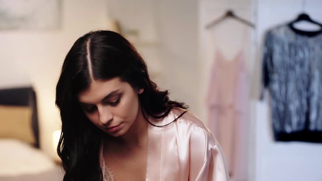 brunette woman in pink satin robe choosing earrings