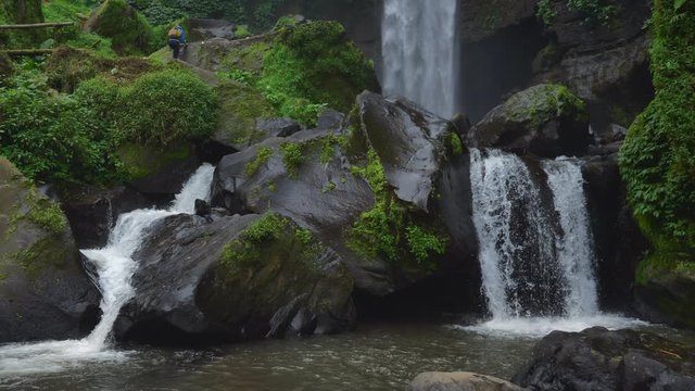Woman walks through the waterfall Coban Talun in Java island, Indonesia