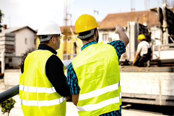 Men in hardhat and green jacket posing on building site.