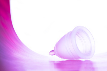 Pink reusable menstrual cup on a white background in lilac neon light.