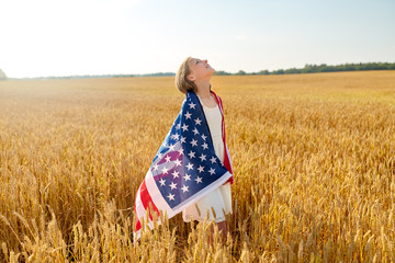 patriotism, independence day and country concept - happy smiling young girl wrapped into national american flag on cereal field looking up