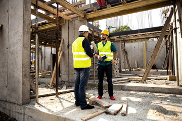 Men in hardhat and green jacket posing on building site.