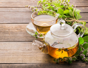 Tea with fresh leaves of lemon balm mint in a cup and teapot on a wooden rustic background. Healing...