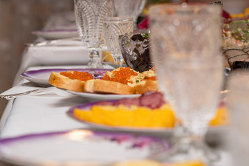Festive table setting with crystal glasses and plates. Sandwiches with red caviar on the table. Selective focus