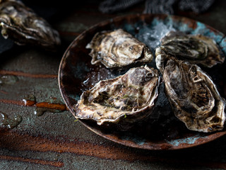 Opened fresh oysters on a dark background, a knife and water drops.