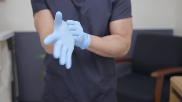 Close up, male nurse puts on disposable gloves in patient hospital room