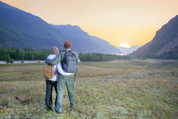 Men and women wearing backpacks enjoying sunset during hike on mountain. Couple embracing hiking active lifestyle.