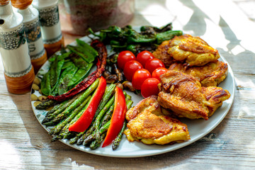 Fried pieces of chicken with vegetables, on a beautiful dish. Stands on a natural wood tabl