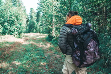 A man with a large tourist backpack traveling through the woods, ecotourism concept.