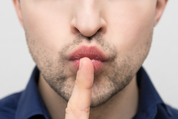 Obraz premium Emotions on the face of a beautiful man, guy holding index finger at her lips, close up