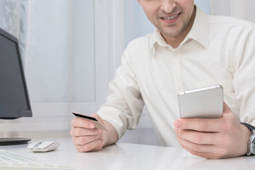 Businessman working in the office, holding a plastic card and smart phone, front view