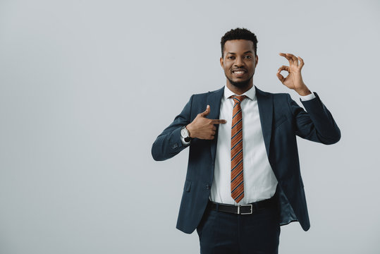 happy african american man pointing with finger at ok sign isolated on grey