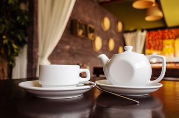 White cup of tea and teapot on a table in a cafe. The concept of tea drinking, relaxation.