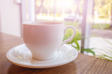 Americano coffee in a white cup on a wooden table against the background of a window, behind which trees. On a horse are plants. Cozy minimalistic still life.