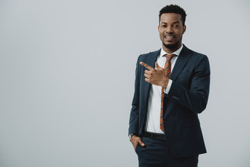 happy african american man pointing with finger isolated on grey